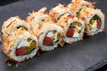 Japanese food, sushi roll  with salmon, sesame seeds, red caviar on black stone.