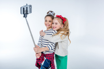 side view of stylish happy girls making selfie on grey