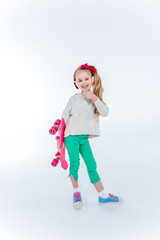 stylish smiling girl in headphones with skateboard listening music on grey