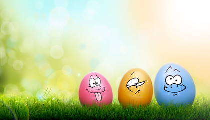 Colourful painted Easter Eggs with a family of cartoon funny faces on green grass and blurred garden and sky background.