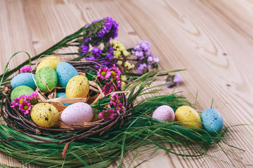 Fototapeta na wymiar Happy Easter. Easter background. Bright colorful eggs in nest with spring flowers over wooden dark background. Selective focus with copy space.