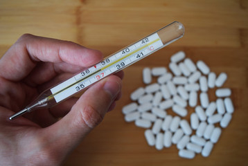 Thermometer with a temperature of 37 celsius degrees in hand and white  pills on a bamboo board background