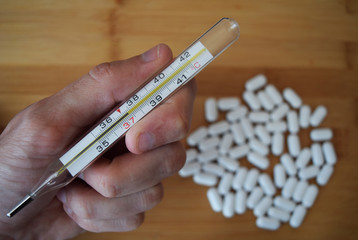 Thermometer with a temperature of 37 celsius degrees in hand and white  pills on a bamboo board background