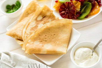 Thin crepes with fresh kiwi, orange, sicilian orange, honey, cream and mint leaves on white rustic wooden table. Selective focus
