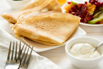 Thin crepes with fresh kiwi, orange, sicilian orange, honey, cream and mint leaves on white rustic wooden table. Selective focus
