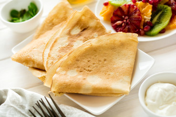 Thin crepes with fresh kiwi, orange, sicilian orange, honey, cream and mint leaves on white rustic wooden table. Selective focus
