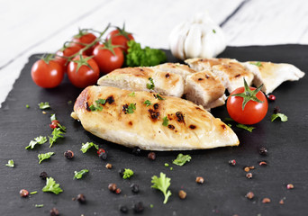 Grilled chicken breast on a slate plate with herbs and cherry tomatoes, garlic and peppercorns. Healthy eating scene, barbecue chicken.