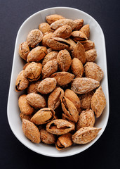 salted almonds in shell on white plate on black slate background