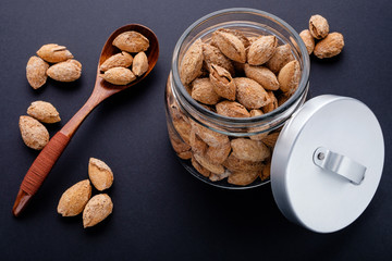 salted almonds in shell in glass jar and spoon on black slate