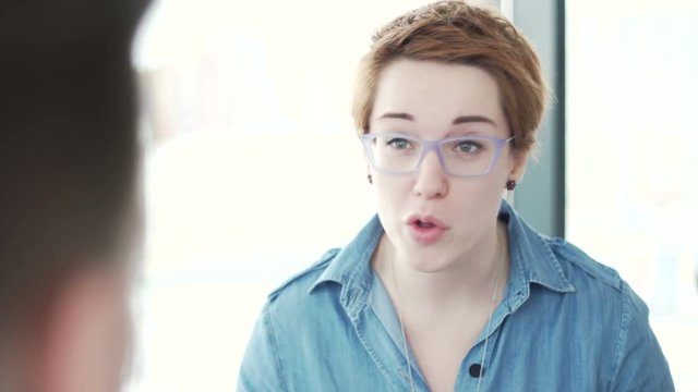 over the shoulder view of angry annoyed woman with red short hair speaking emotionally and strictly during the meeting interview with the assistant in the light office