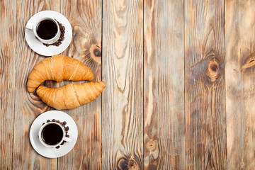Two cups of coffee and a croissant on a wooden table