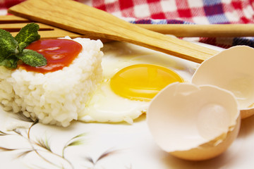 Rice with fried egg and tomato on the tablecloth with wooden cutlery