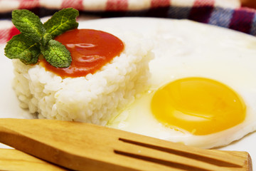 Rice with fried egg and tomato on the tablecloth with wooden cutlery