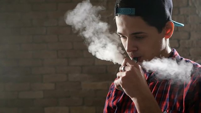 Boy starts vaping using an e-cigarette and sending thick smoke through his mouth