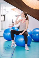 Fototapeta na wymiar Young woman sitting on pilates balls , resting from training and drinking water