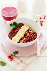 Healthy breakfast: muesli with walnuts, milk, honey, banana, orange and garnet seeds on white wooden background. Selective focus
