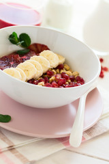 Healthy breakfast: muesli with walnuts, milk, honey, banana, orange and garnet seeds on white wooden background. Selective focus
