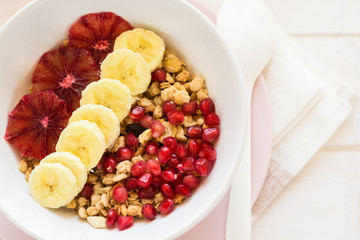 Healthy breakfast: muesli with walnuts, milk, honey, banana, orange and garnet seeds on white wooden background. Selective focus
