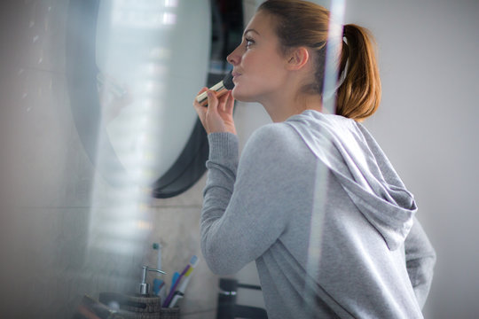 Young adult female putting make-up on in bathroom mirror