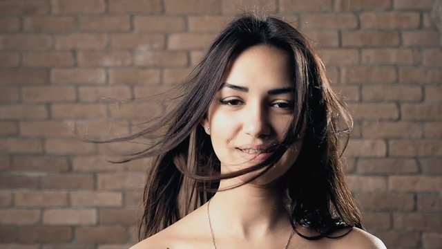 Young girl with streaming loose brown hair and open shoulders smiles in slo-mo