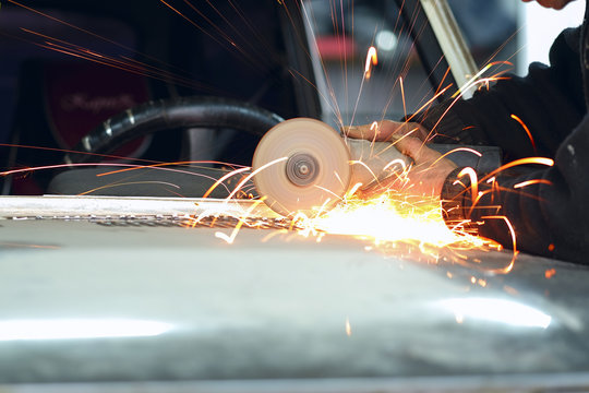 Worker works with angle grinder in a car repair shop