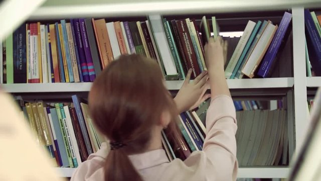 Portrait of a pretty college girl picking up books from bookcase