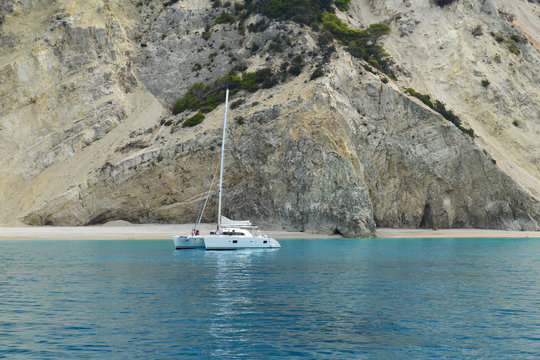 Catamaran anchored in calm turquoise sea near vertical cliffs and sandy beach