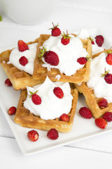 waffles with wild strawberries and whipped cream on white table