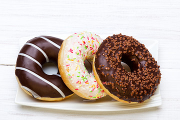 Tasty donuts with icing and chocolate on white wooden background, copy space