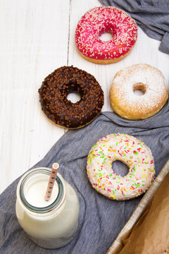 Bottle of milk and colorful donuts with chocolate and icing, selective focus
