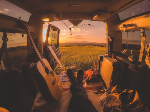 Man lying in camper van with guitar, looking at sunset and field 
