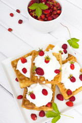 waffles with wild strawberries and whipped cream on white table