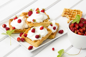 waffles with wild strawberries and whipped cream on white table