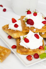 waffles with wild strawberries and whipped cream on white table
