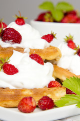 waffles with wild strawberries and whipped cream on white table