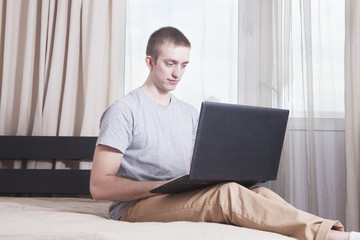 Young man with laptop sitting on bed. Working from home