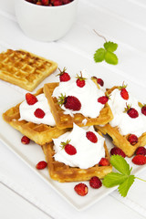 waffles with wild strawberries and whipped cream on white table