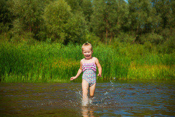 Cute little girl runs in warm water in river on a hot sunny day