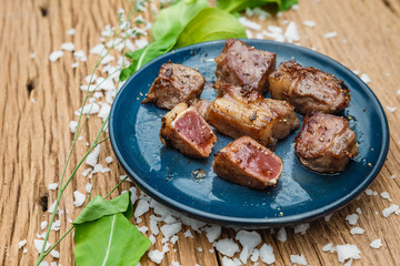 Medium Rare Fried Diced Marinated Beef on Blue Ceramic Plate on Wood Panel with Sea Salt and Vegetable Decorated.