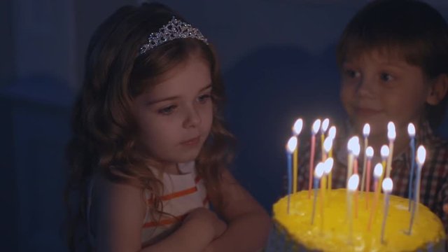 A little girl looks at candles on a festive cake and makes a wish in Slow motion