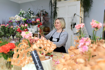 Kobieta w kwiaciarni układa bukiet z kolorowych kwiatów.