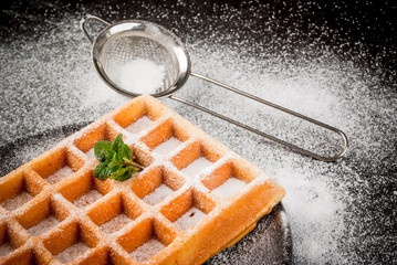 Freshly baked Belgian waffles, sprinkled with powdered sugar. On a black plate on a black stone table. Close view, copy space