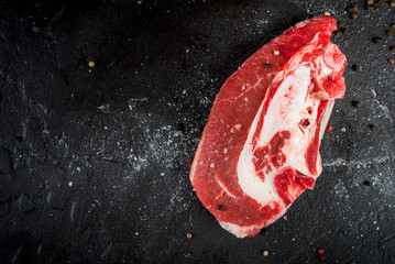 Fresh uncooked raw meat beef brisket on the bone. On black concrete kitchen table with spices for...