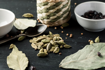 Pile of cardamon seeds among other condiments and kitchen stuff on a black wooden table