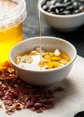 Thin honey trickle poured in white bowl full of raw peanuts, vertical