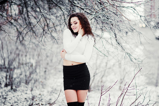 Curly brunette girl background falling snow, wear on black mini skirt and wool stockings. Model on winter. Fashion portrait at snowy weather. Instagram toned photo.