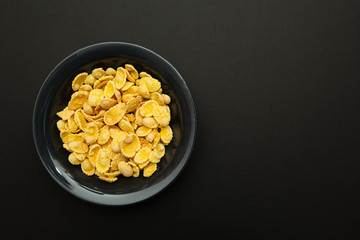 Yellow corn flakes in a black plate on a pink background.