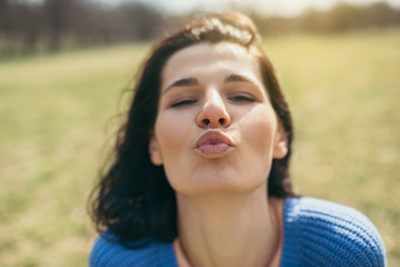 Fototapeta na wymiar Close up portrait of attractive happy young woman being playful and carefree with beautiful kiss on sunny day. Lifestyle concept. Happy female portrait on summer or spring day outside in park. Fun day