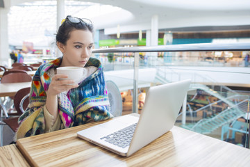 Beautiful woman in a restaurant drinking coffee in the morning and having fun looking at the laptop screen.