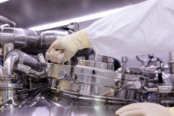 A man opens a chemical reactor. Rector of the pharmaceutical industry. The man closes the reactor. Production of granulate, suspension for tablets.
